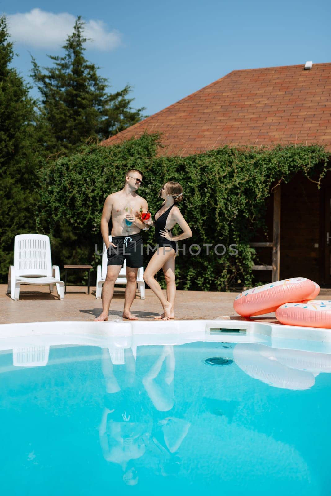 guy and a girl in bathing suits are relaxing, sunbathing and having fun near the blue pool