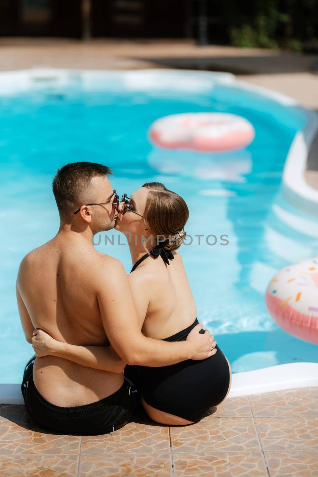 guy and a girl in bathing suits are relaxing, sunbathing and having fun near the blue pool