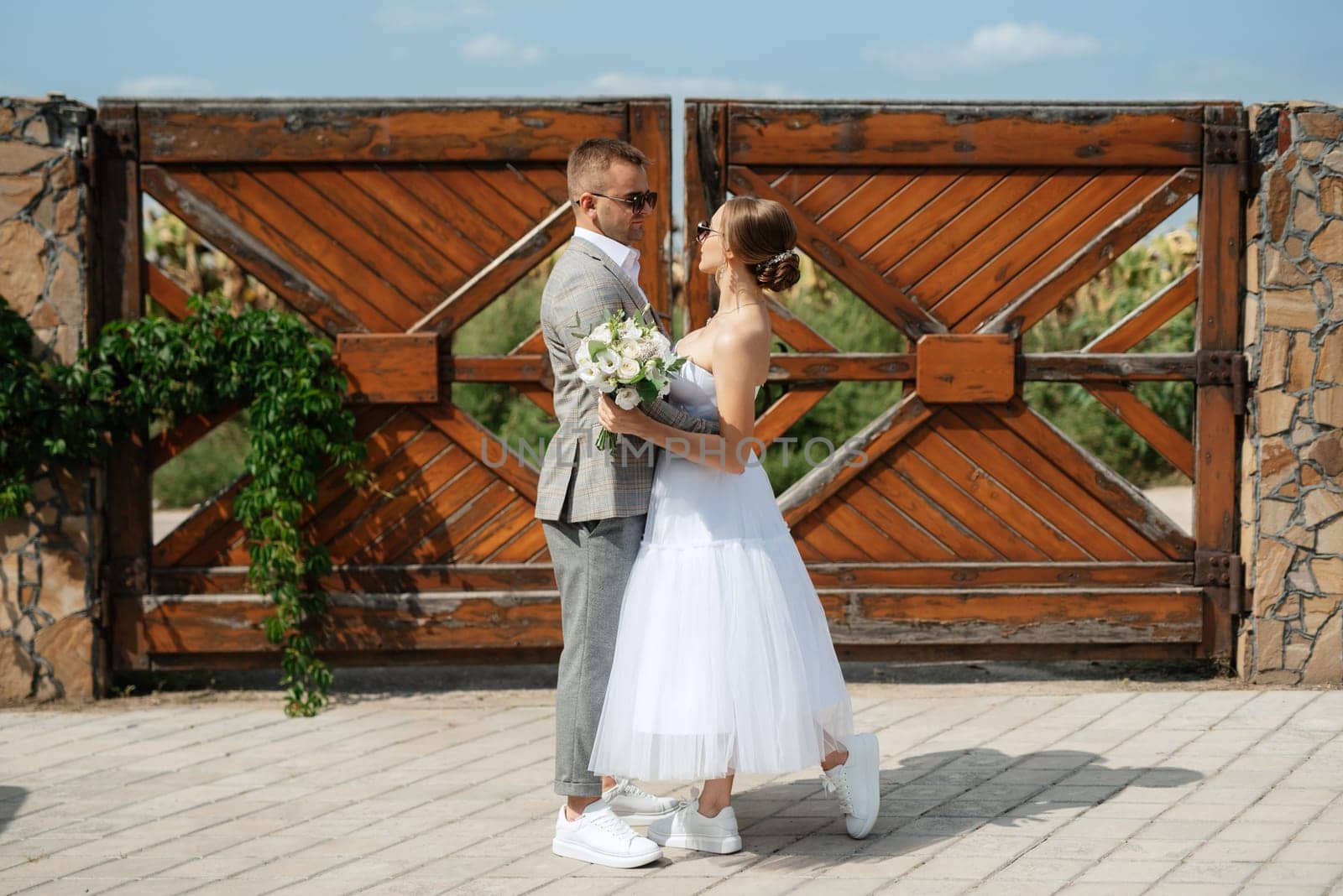 young couple bride in a white short dress and groom in a gray suit near the wooden gate by Andreua