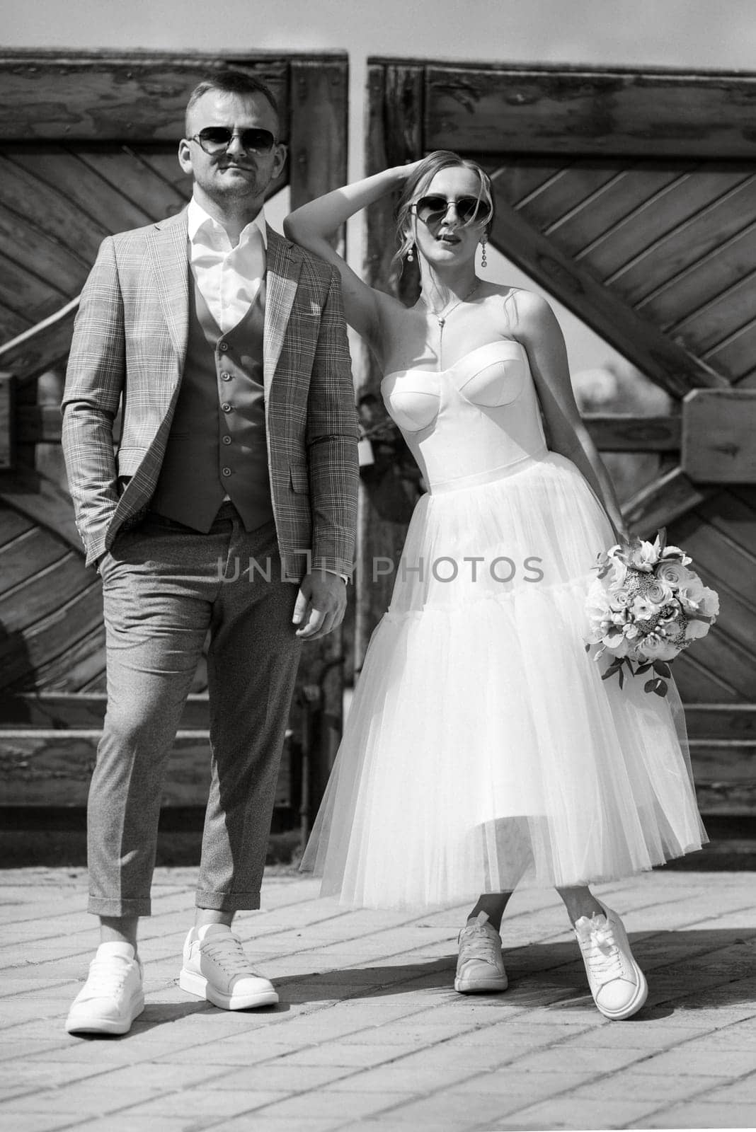 young couple bride in a white short dress and groom in a gray suit near the wooden gate by Andreua