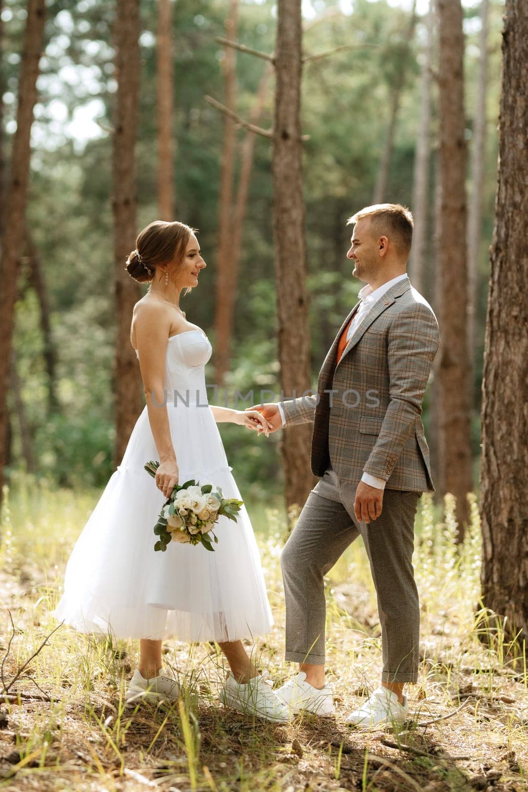 young couple bride in a white short dress and groom in a gray suit in a pine forest by Andreua