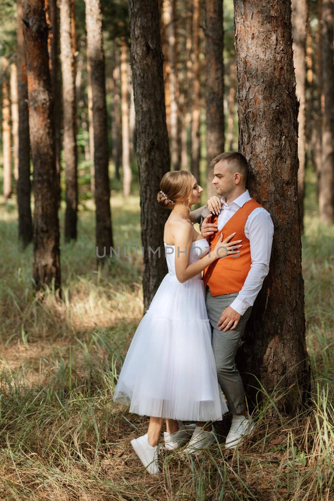 young couple bride in a white short dress and groom in a gray suit in a pine forest by Andreua