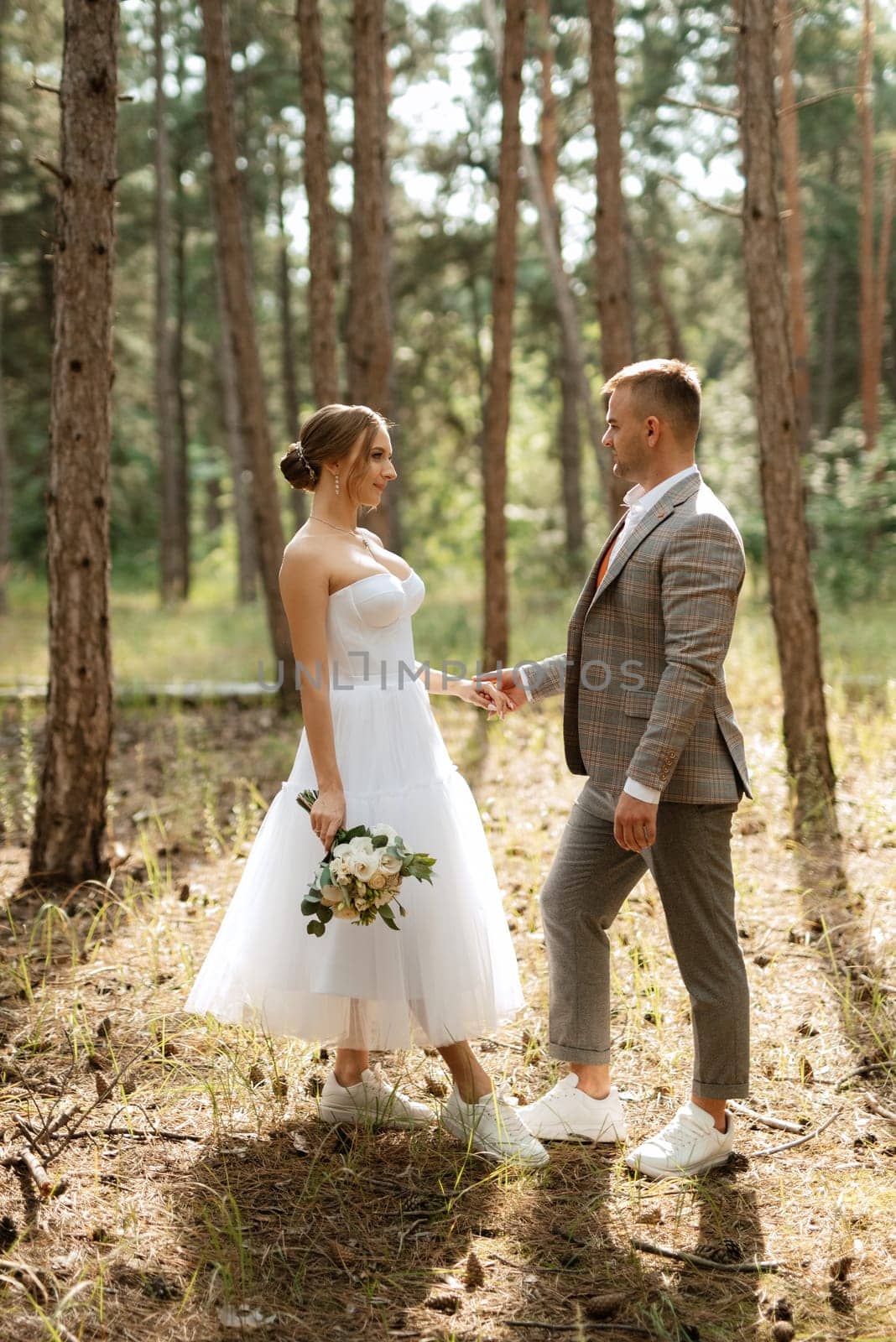 young couple bride in a white short dress and groom in a gray suit in a pine forest among the trees