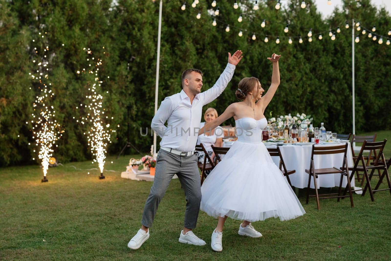 the first dance of the groom and bride in a short wedding dress on a green meadow