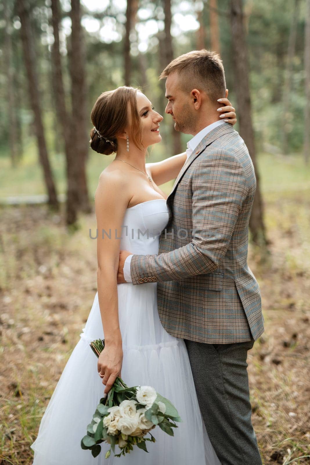 young couple bride in a white short dress and groom in a gray suit in a pine forest by Andreua