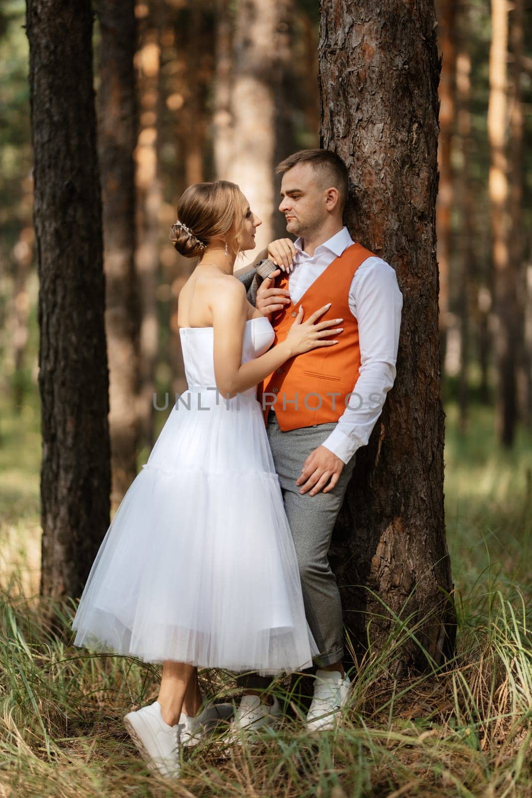 young couple bride in a white short dress and groom in a gray suit in a pine forest among the trees