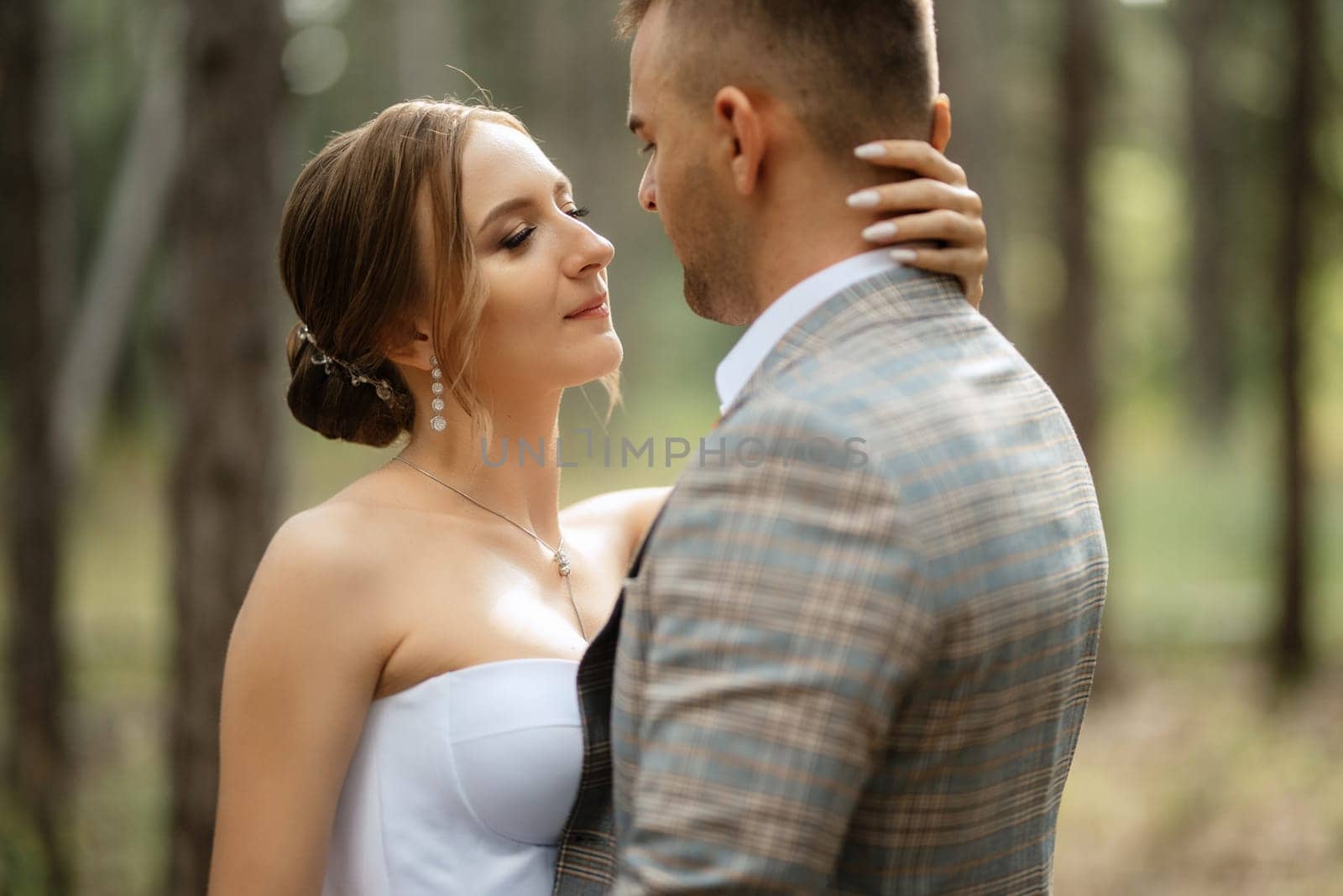 young couple bride in a white short dress and groom in a gray suit in a pine forest by Andreua