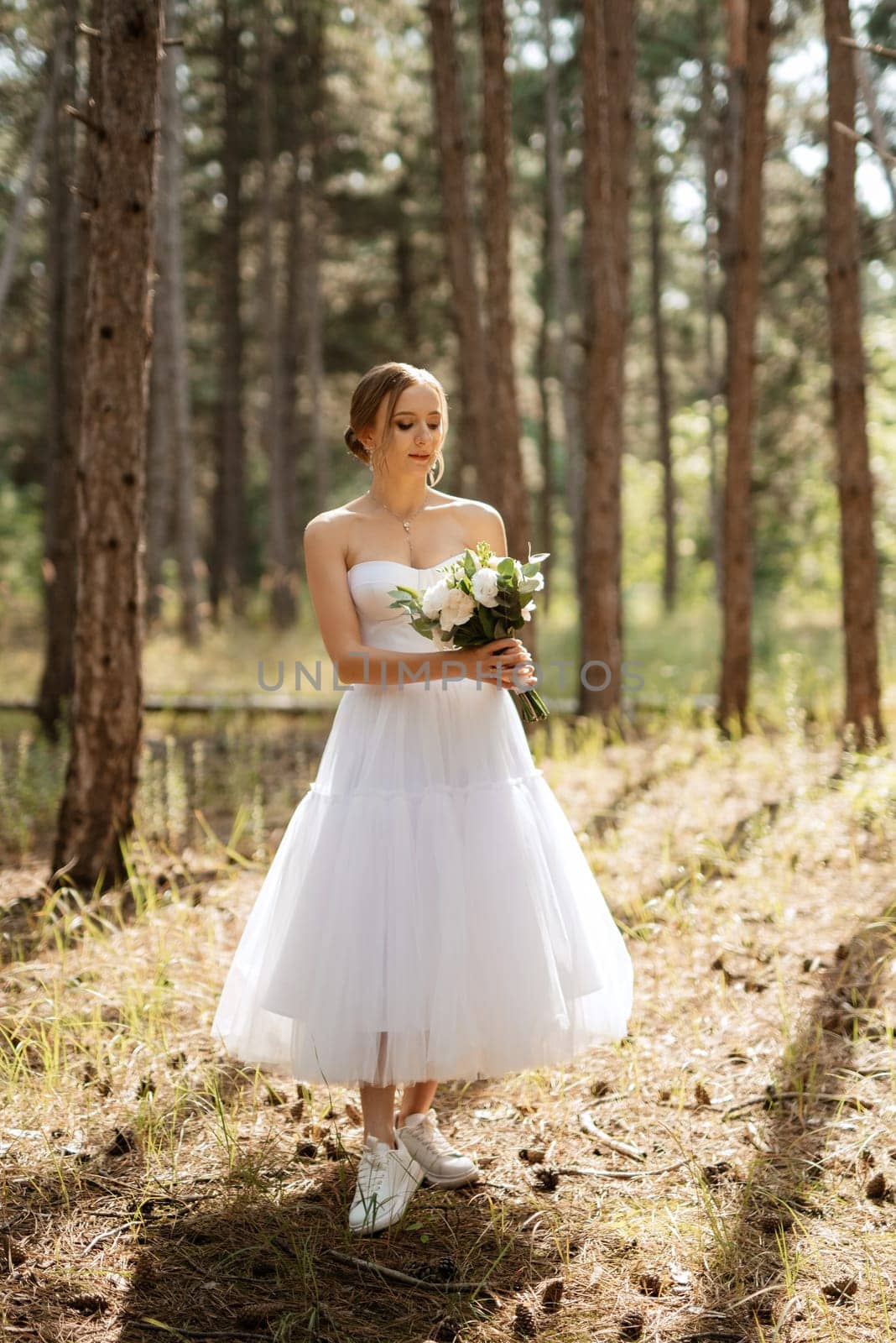 young bride in a white short dress in a spring pine forest among the trees