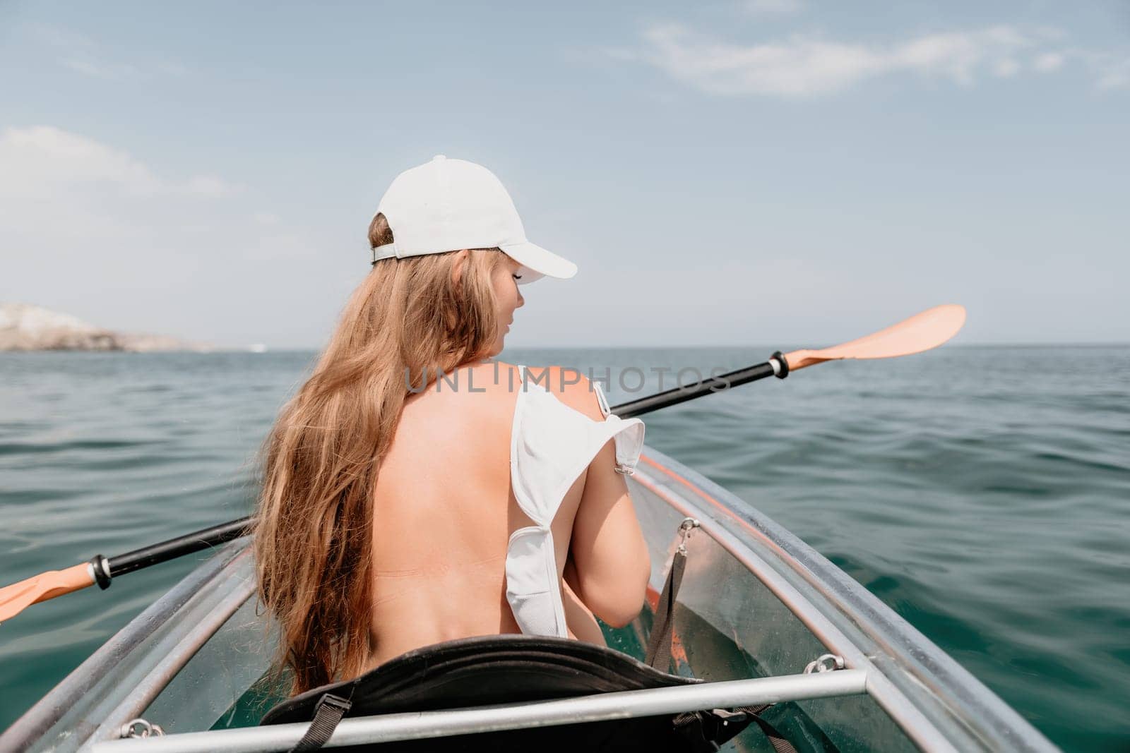 Woman in kayak back view. Happy young woman with long hair floating in transparent kayak on the crystal clear sea. Summer holiday vacation and cheerful female people having fun on the boat.