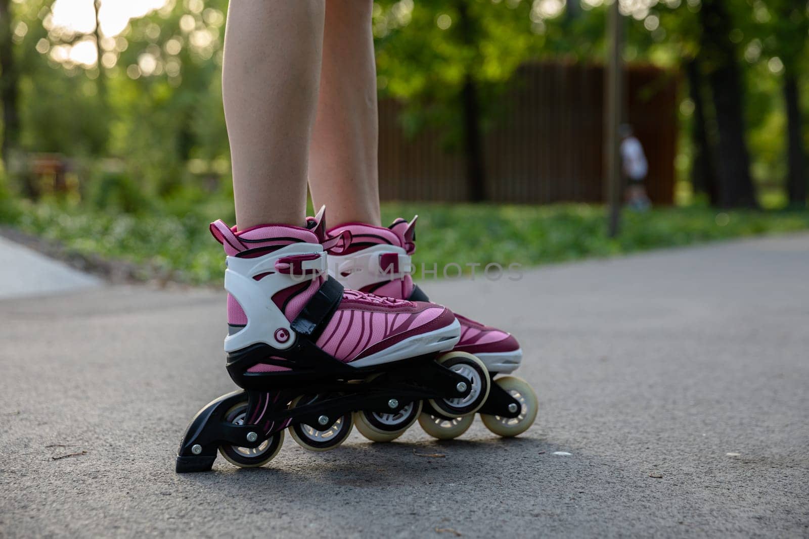 Spending time in a green city park. Close-up of a woman's legs. Woman wearing rollerblades. Playing sports in a city park. A girl rollerblades on an asphalt alley.