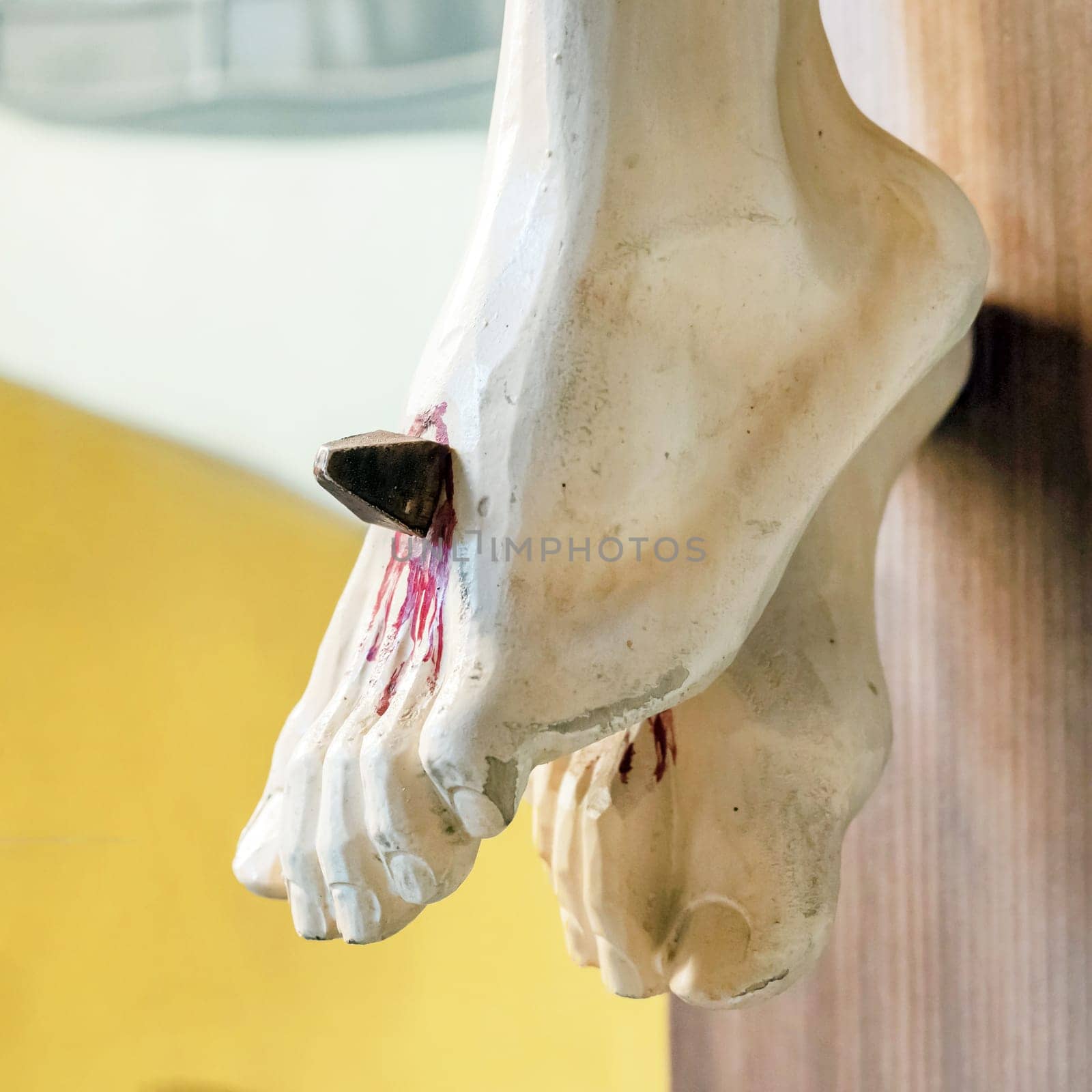 Nailed feet, detail of wooden statue of Jesus Christ crucified in a defocused background.