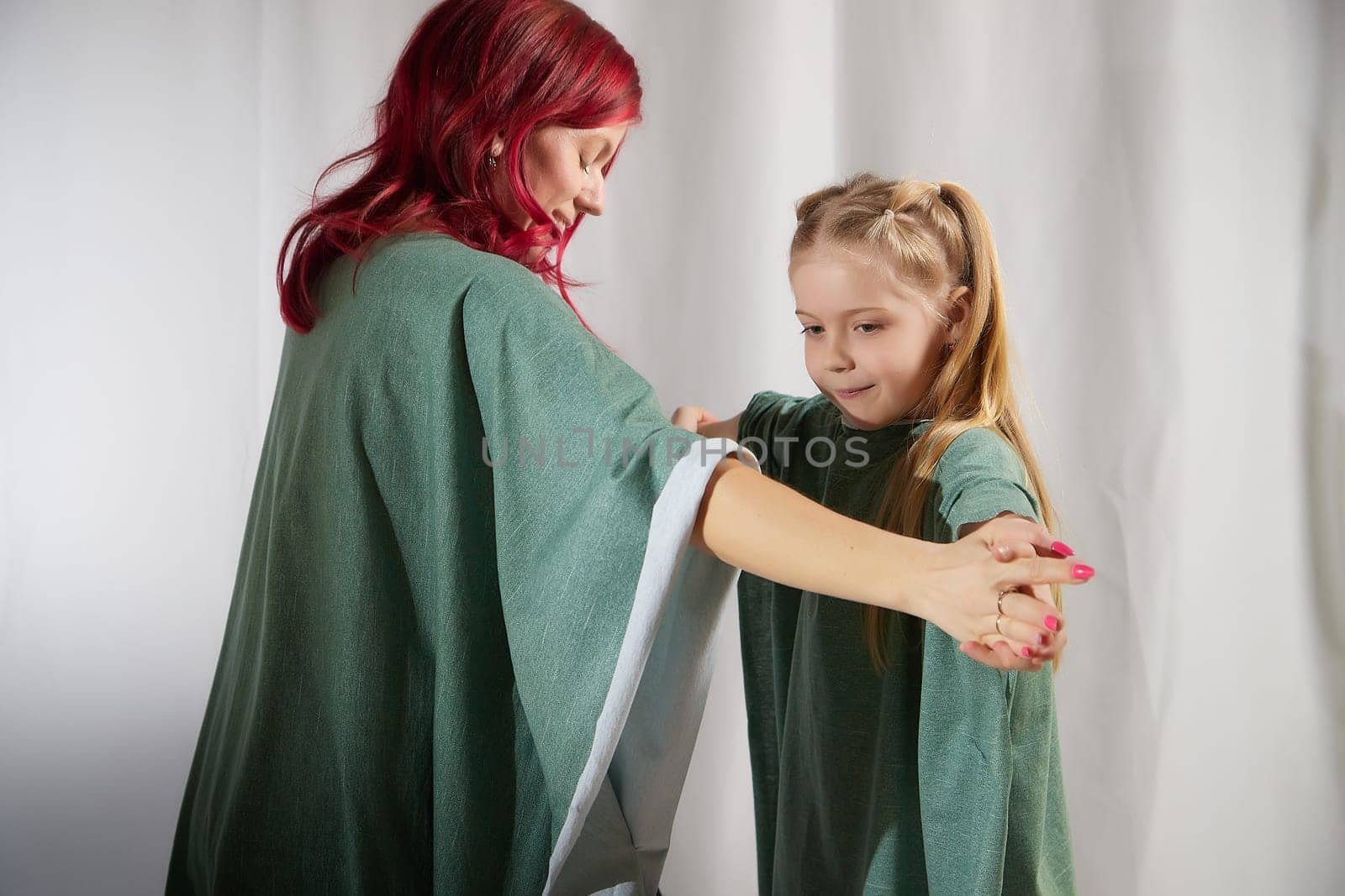 Amazing pretty mother and daughter having fun and dacncing together. Red haired mom and small little blonde girl hugging and having lovely free time on white background by keleny