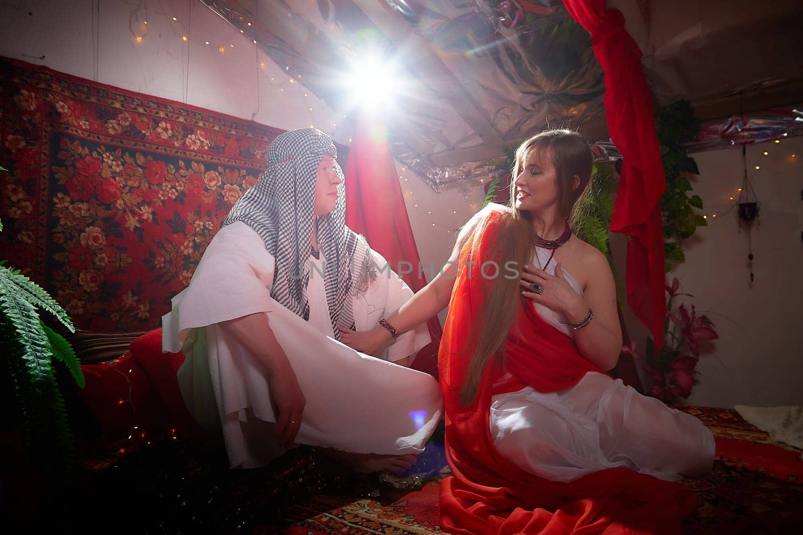 Portrait of young arabian muslim couple in traditional clothes in cozy red room. Fhoto shoot in easten style with male and female model like in a harem with a sultan and an odalisque. Partial focus by keleny