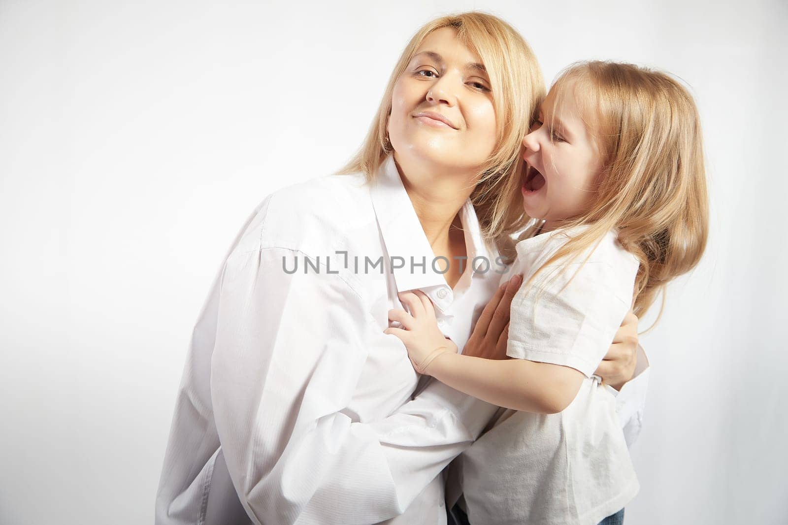 Portrait of a mother and daughter, where a little girl screams at an adult woman on a white background. The concept of a capricious child and behavior in the family. Angry teen and calm lady by keleny