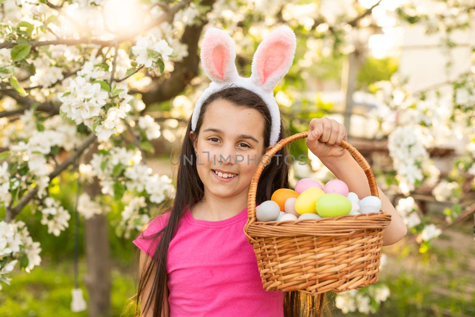 A little girl with pink rabbit ears. painted eggs in the park. Easter. Copy space