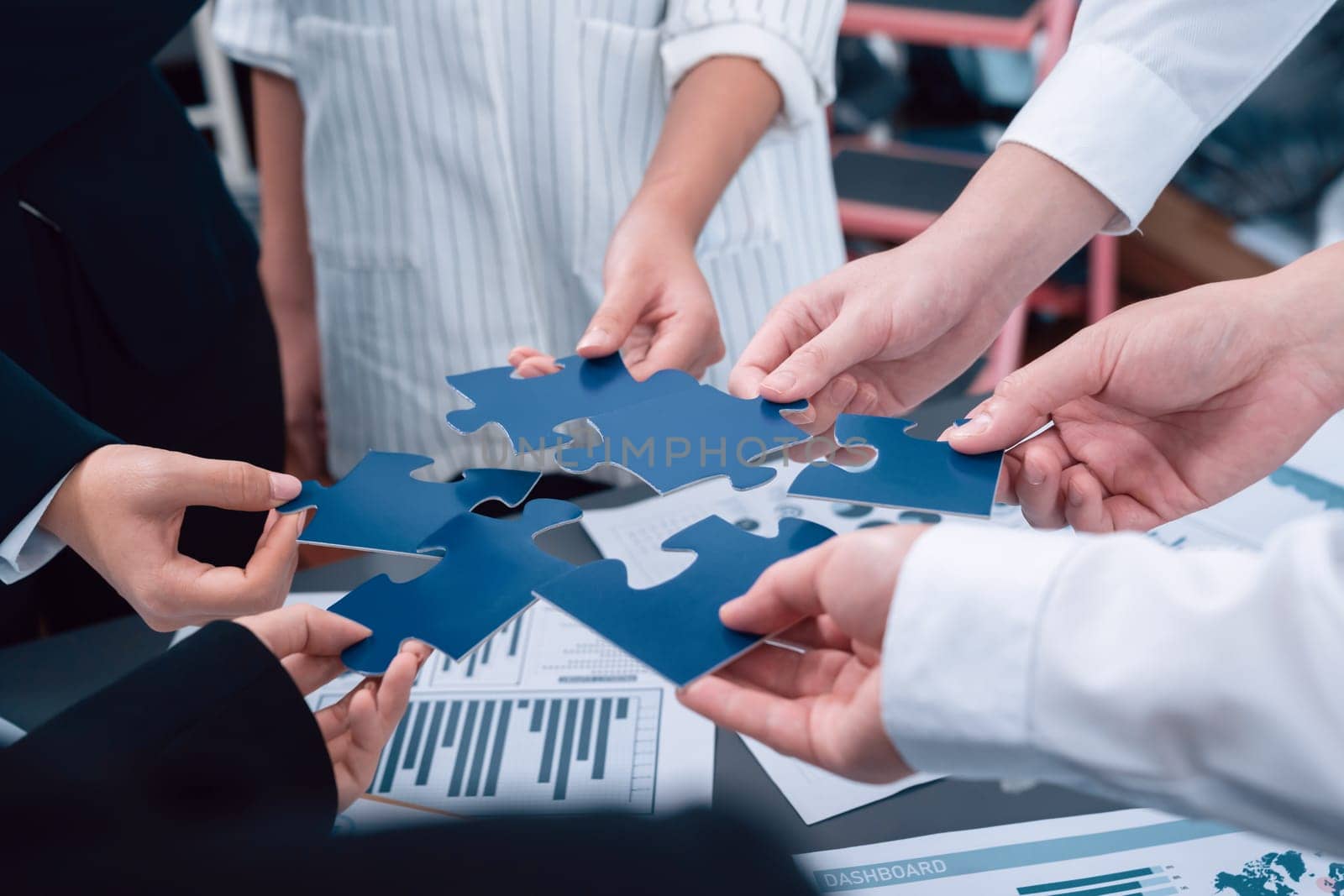 Closeup top view business team of office worker putting jigsaw puzzle together over table filled with financial report paper in workplace with manager to promote harmony concept in meeting room.