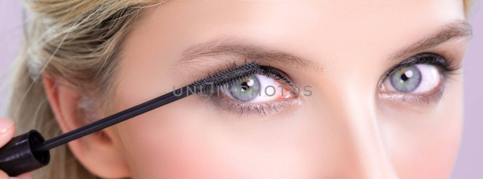 Closeup woman with blond hair putting alluring black mascara with brush in hand on long thick eyelash. Perfect fashionable cosmetic clean facial skin with beautiful eye young woman in high resolution.