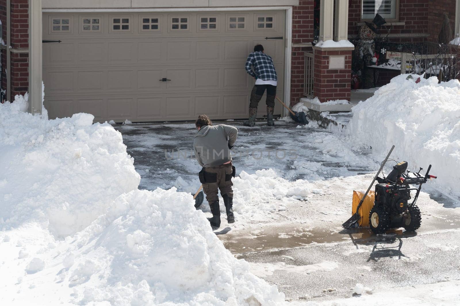 Two young guys finish clearing snow in front of the garage