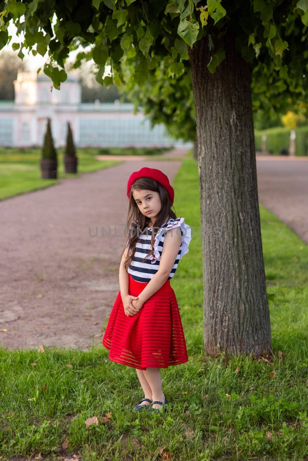 A little brunette girl, dressed in a French style, stands in park by Zakharova