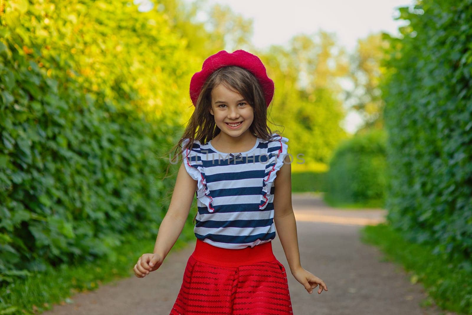A portrait of a beautiful brunette in a red beret, red skirt, and a striped T-shirt runs among green leaves in the park. Copy space