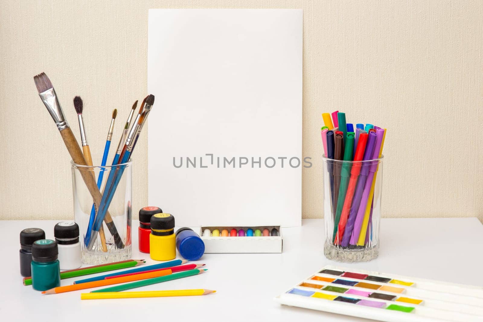 White paper, paintbrushes and colorful drawing supplies on white table: watercolors,pastel crayons, pencils , acrylic paints. Mock up