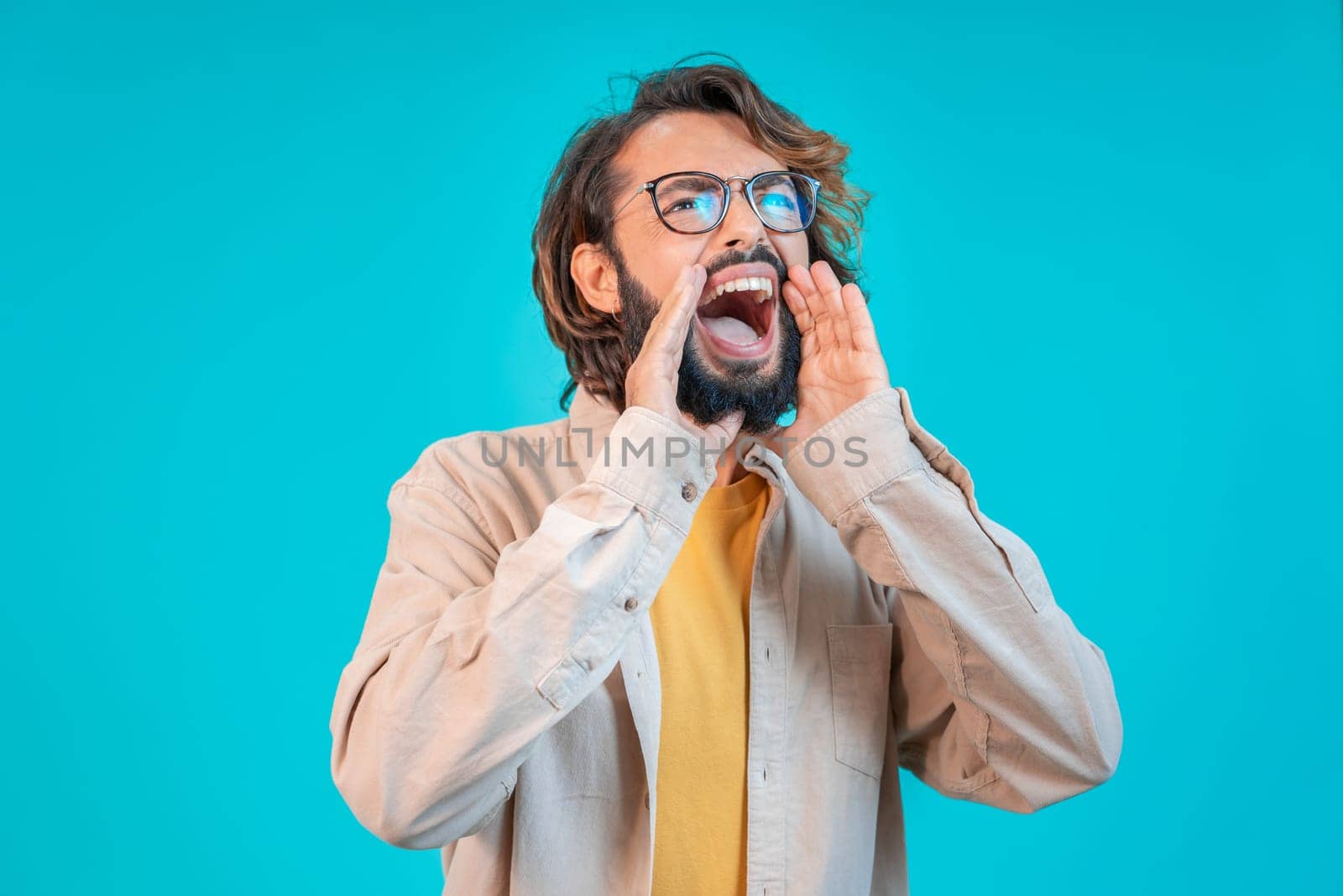 Man shouting loud calling attention with hands like megaphone isolated on blue studio background by PaulCarr