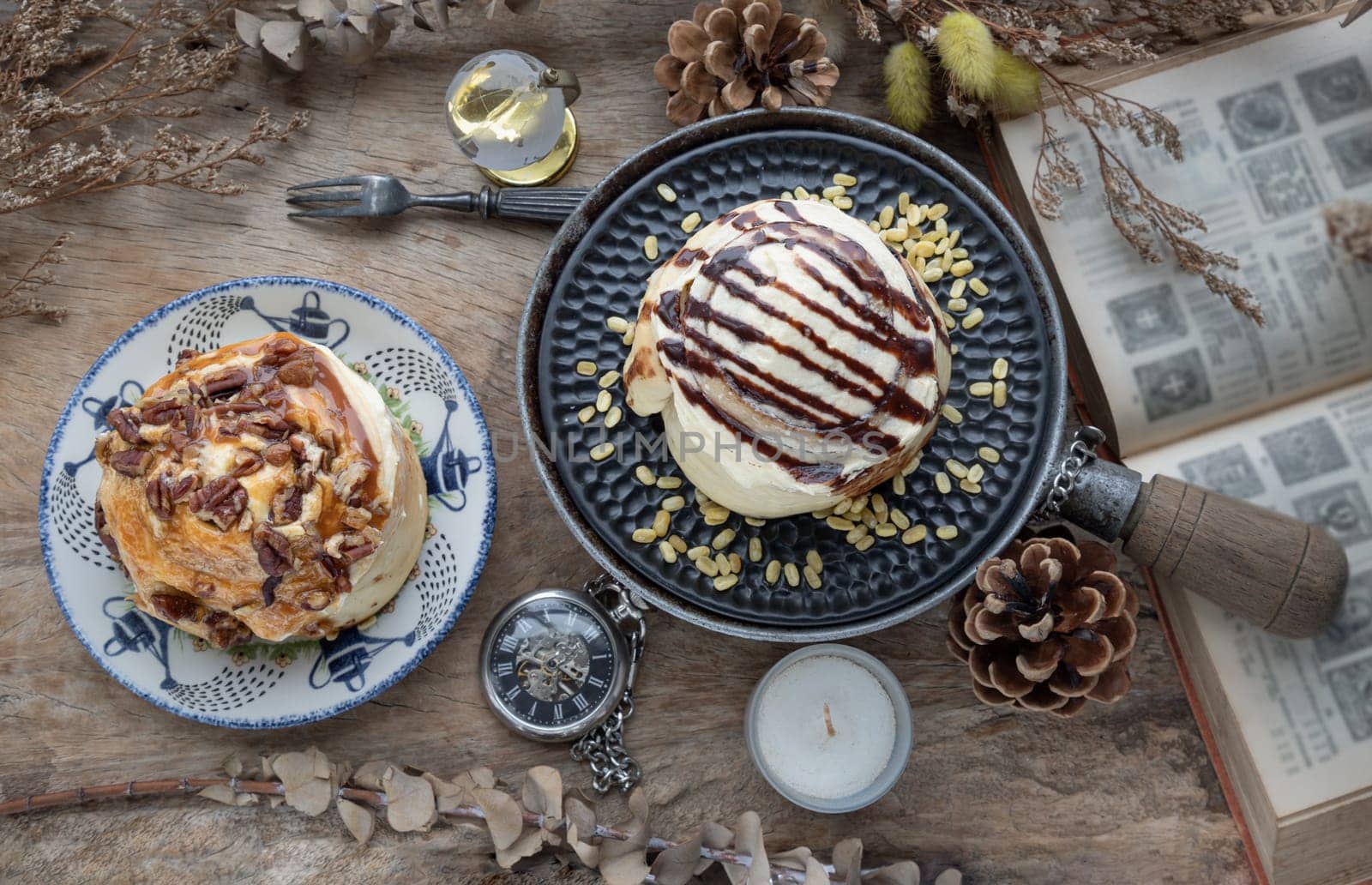 Two Homemade Soft Chocolate Buns, Cinnamon roll topped with rich cream cheese frosting and Caramel Pecanbon topped with caramel frosting and pecans served with Metal fork on old rustic wooden table. The concept of delicious dessert, Top view, Selective focus.