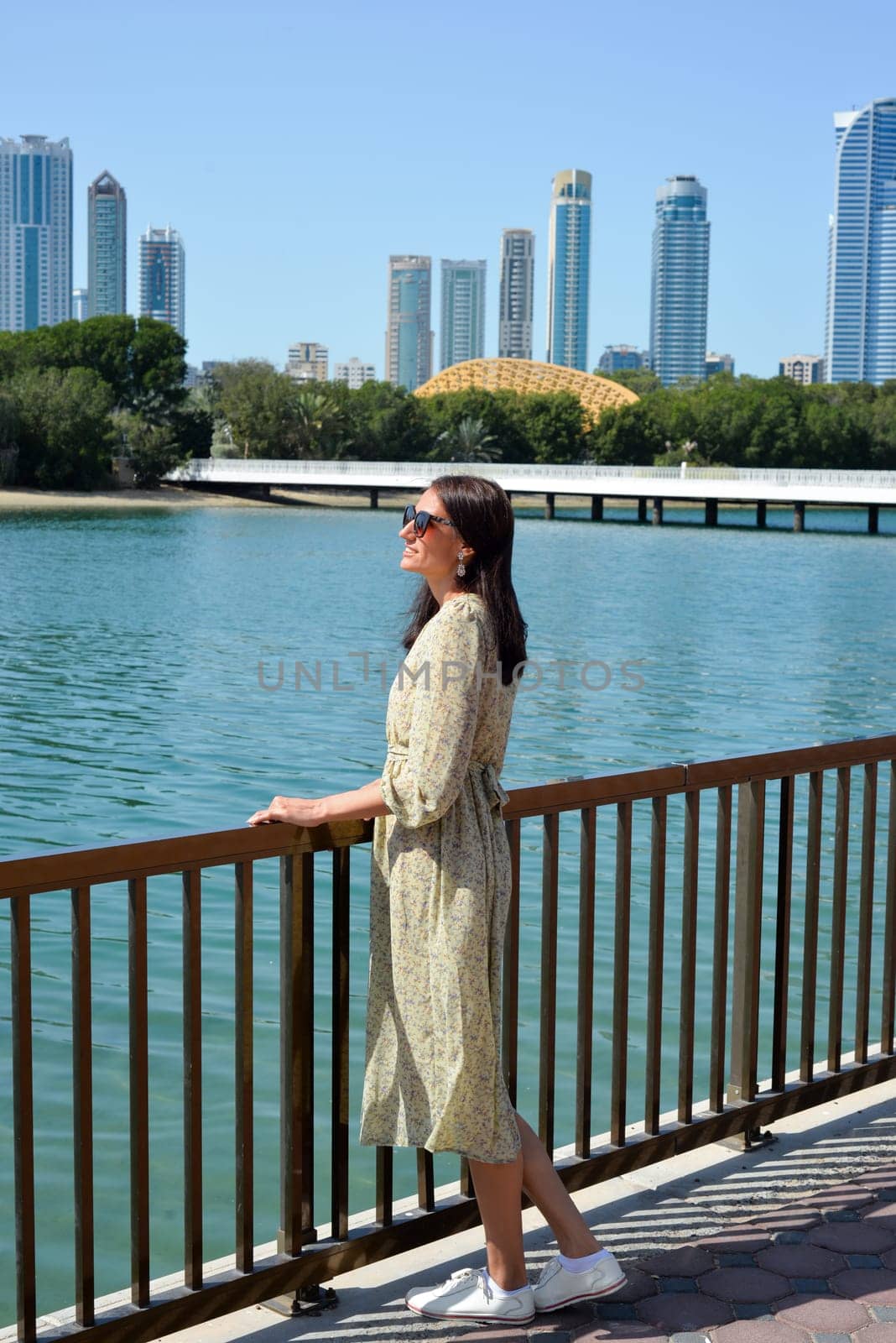 Cityscape of Sharjah UAE. A young woman in a long dress enjoys the view of skyscrapers and relaxing