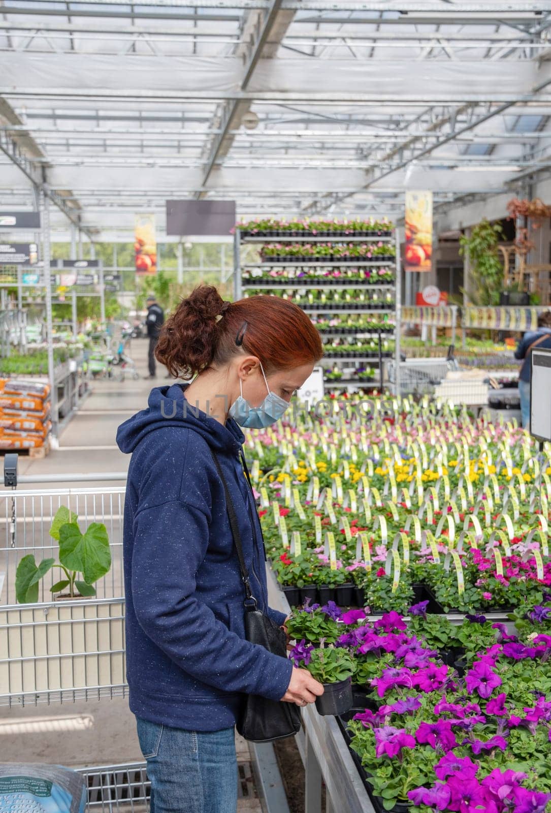 A young woman in a mask chooses and buys seedlings in a garden center with a large assortment of plants, a woman enjoys hobbies and leisure activities, growing plants and flowers in her garden