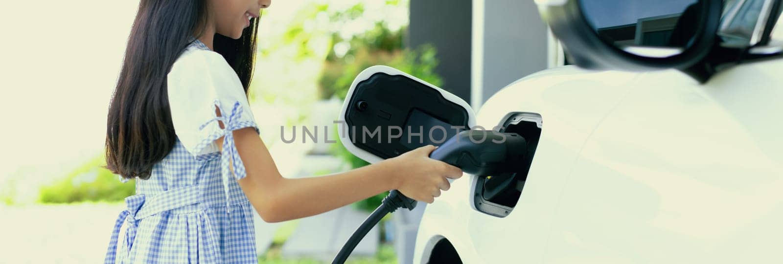 A playful girl holding an EV plug, a home charging station providing a sustainable power source for electric vehicles. Alternative energy for progressive lifestyle.