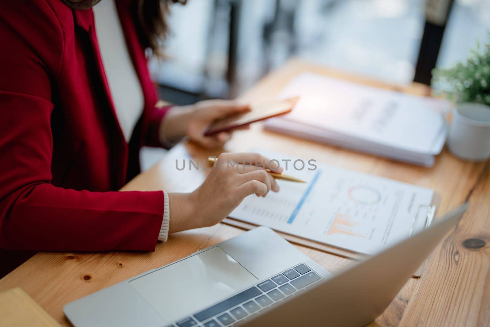 Portrait of a young Asian woman showing a smiling face as she uses her phone, computer and financial documents on her desk in the early morning hours.