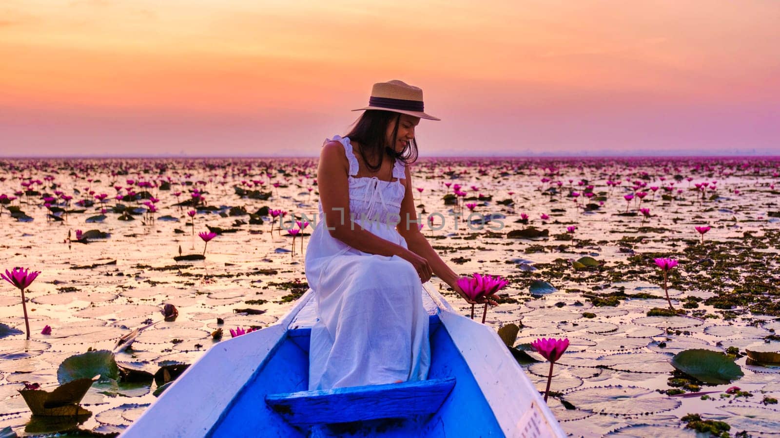 Asian women with a hat and dress in a boat at the Beautiful Red Lotus Sea Kumphawapi is full of pink flowers in Udon Thani in northern Thailand. Flora of Southeast Asia.