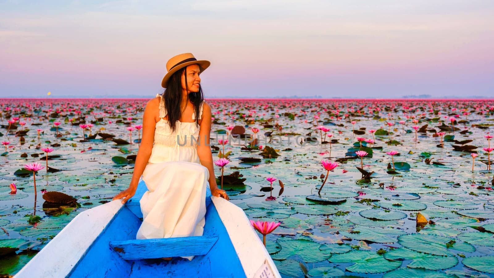 Thai women in a boat at the Beautiful Red Lotus Sea Kumphawapi is full of pink flowers in Udon Thani in northern Thailand. Flora of Southeast Asia.