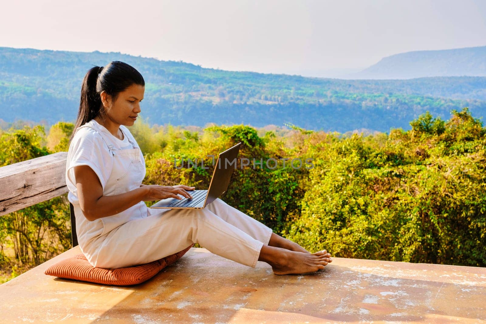 Young woman digital nomad traveler working online using a laptop and enjoying the beautiful natural landscape in front of a tent at sunrise. Digital nomad working on a laptop, remote working