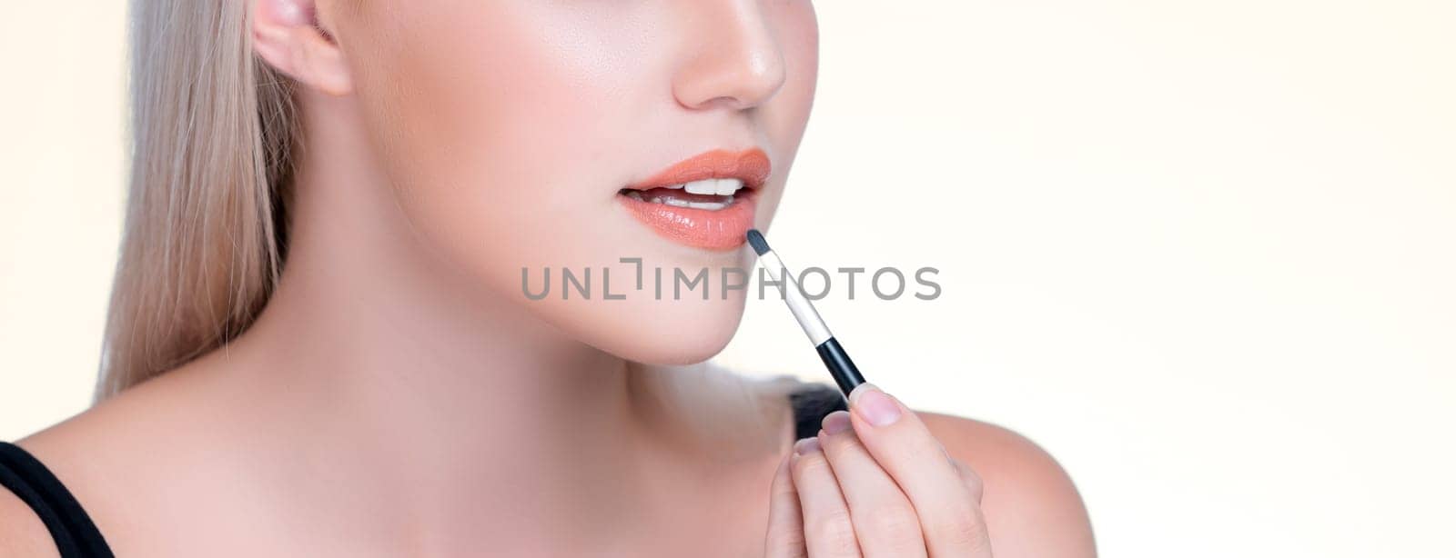 Closeup personable young woman with flawless healthy skin and natural makeup putting fashion glossy lipstick on her lip with lip brush in isolated background. Facial cosmetic makeup in process.