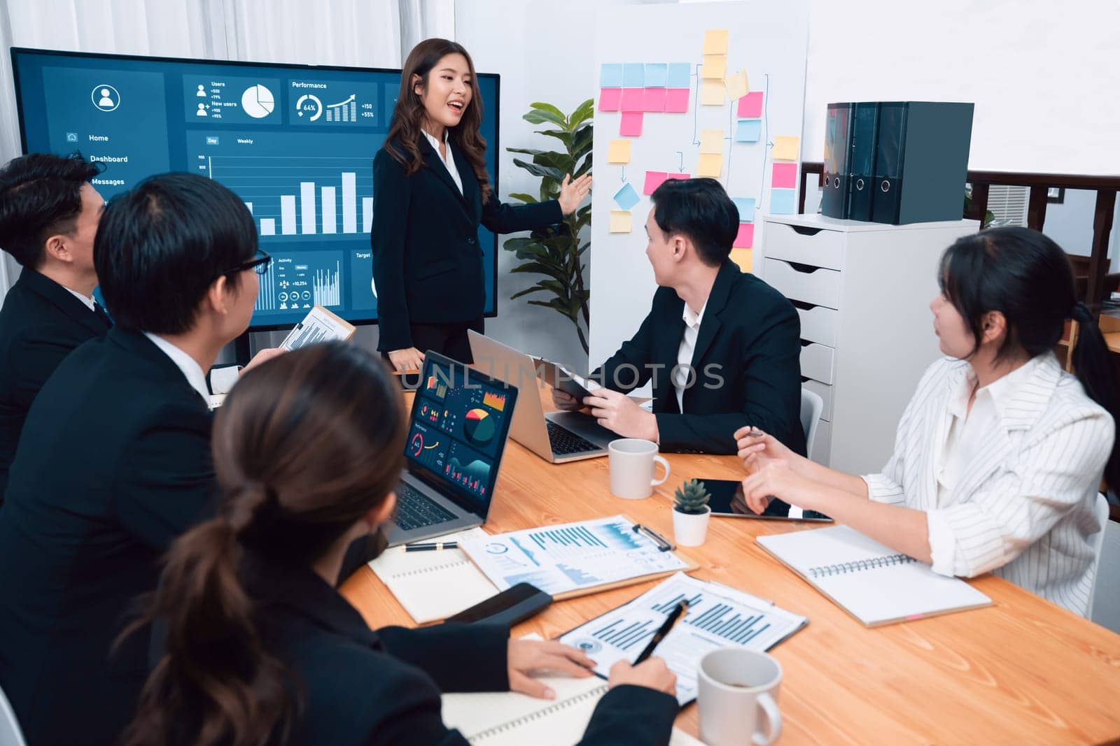 Confidence and young asian businesswoman give presentation on financial business strategy in dashboard report display on screen to colleagues in conference room meeting as harmony in workplace concept