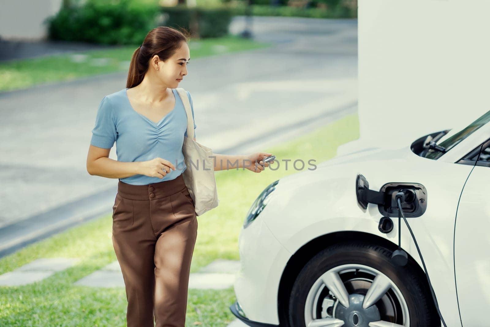 Progressive woman recharge her EV car at home charging station. by biancoblue
