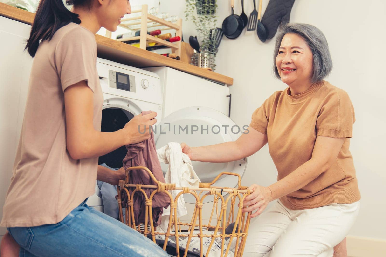 Daughter and mother working together to complete their household chores near the washing machine in a happy and contented manner. Mother and daughter doing the usual tasks in the house.