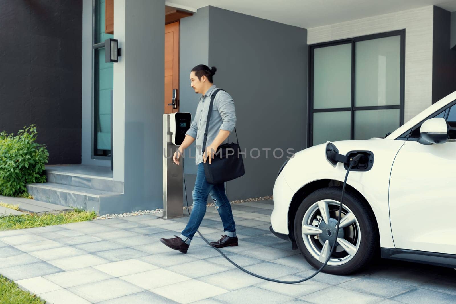 Progressive concept of asian man and electric car with home charging station. by biancoblue