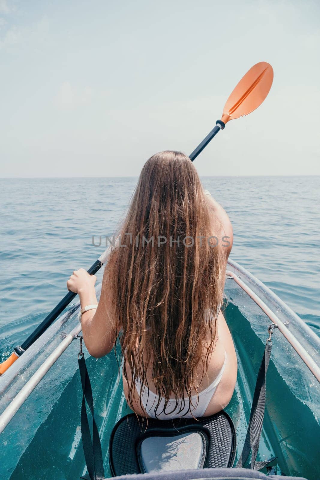 Woman in kayak back view. Happy young woman with long hair floating in transparent kayak on the crystal clear sea. Summer holiday vacation and cheerful female people having fun on the boat.