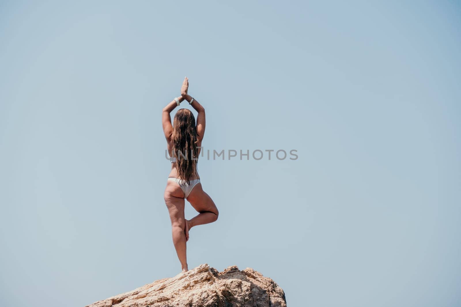Woman meditating in yoga pose silhouette at the ocean, beach and rock mountains. Motivation and inspirational fit and exercising. Healthy lifestyle outdoors in nature, fitness concept.