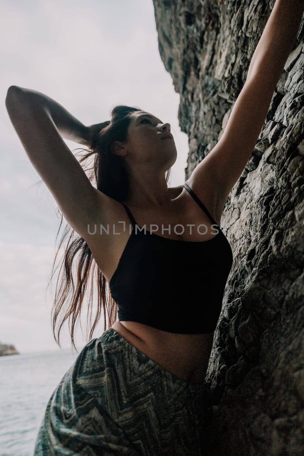 A girl climbs a rock. The athlete trains in nature. Woman overcomes difficult climbing route. Extreme hobby. Tourist woman rock climber hiking on mountains rocks over beautiful sea coast