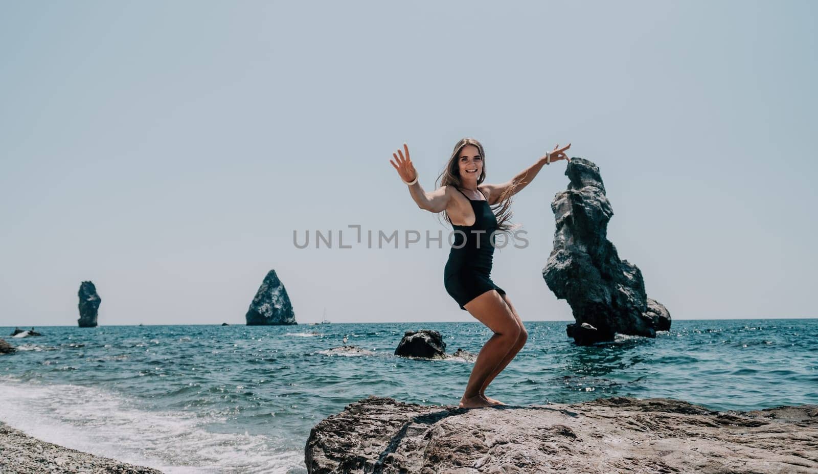 Woman travel sea. Young Happy woman in a long red dress posing on a beach near the sea on background of volcanic rocks, like in Iceland, sharing travel adventure journey