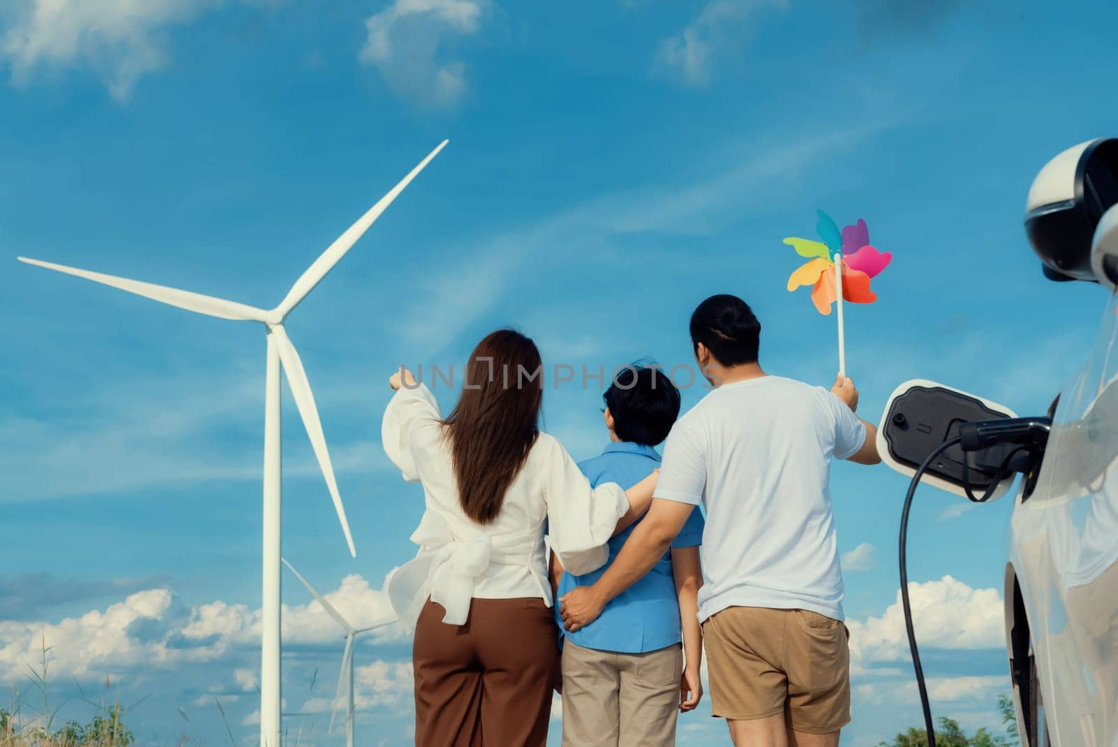 Progressive happy family enjoying their time at wind farm for green energy production concept. Wind turbine generators provide clean renewable energy for eco-friendly purposes.