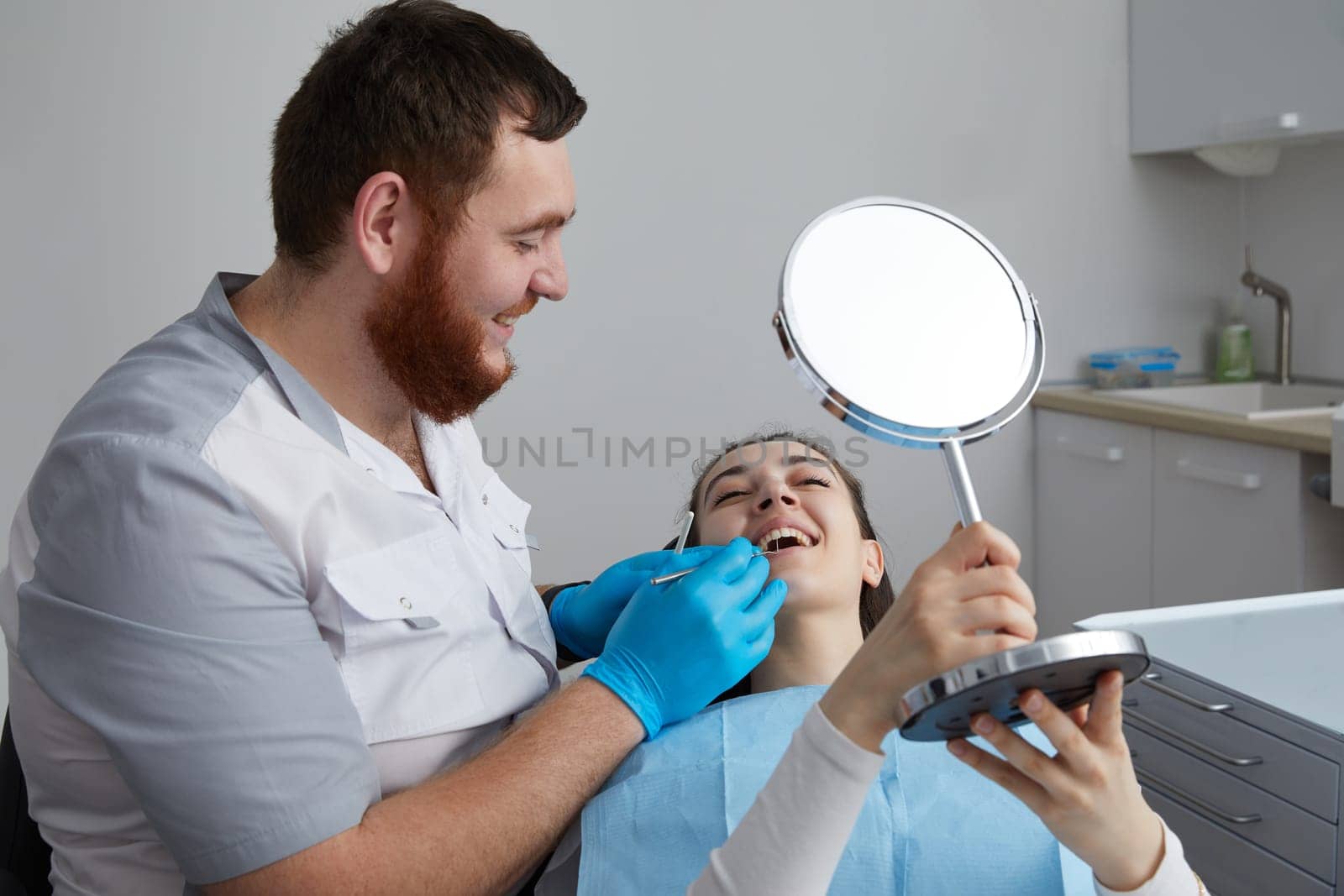Young Woman checking her beautiful smile in mirror after stomatological treatment by Mariakray