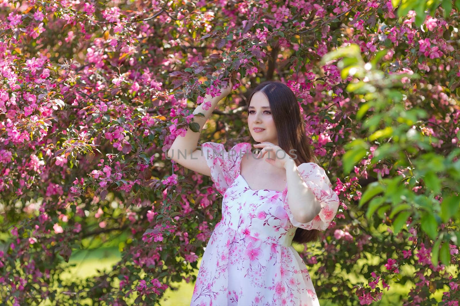 A pretty girl in a light pink dress standing near pink blooming trees, in the garden. Close up. Copy space
