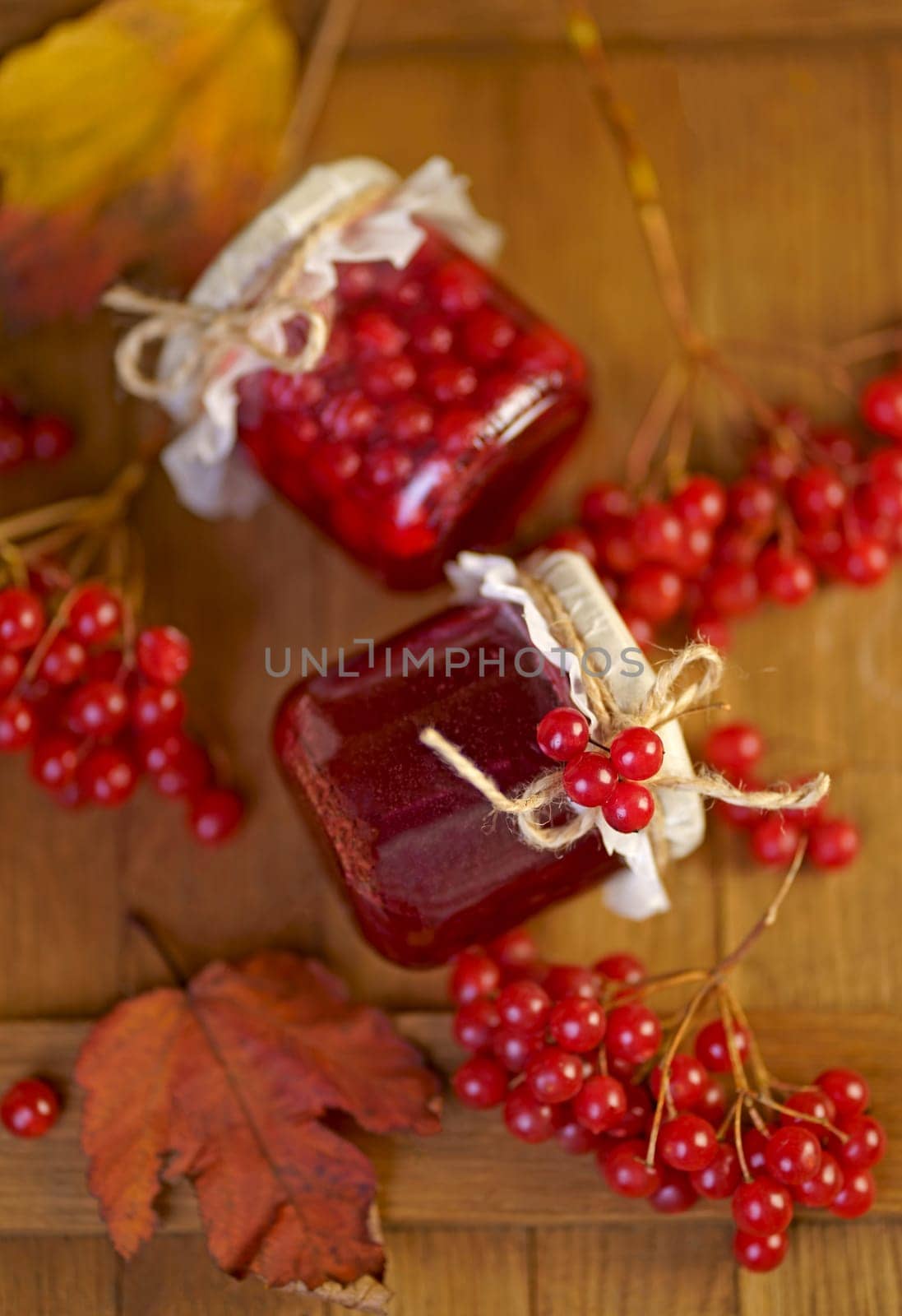 Home preparations. Viburnum jam in a glass jar on a wooden table near fresh viburnum berries and autumn berries by aprilphoto