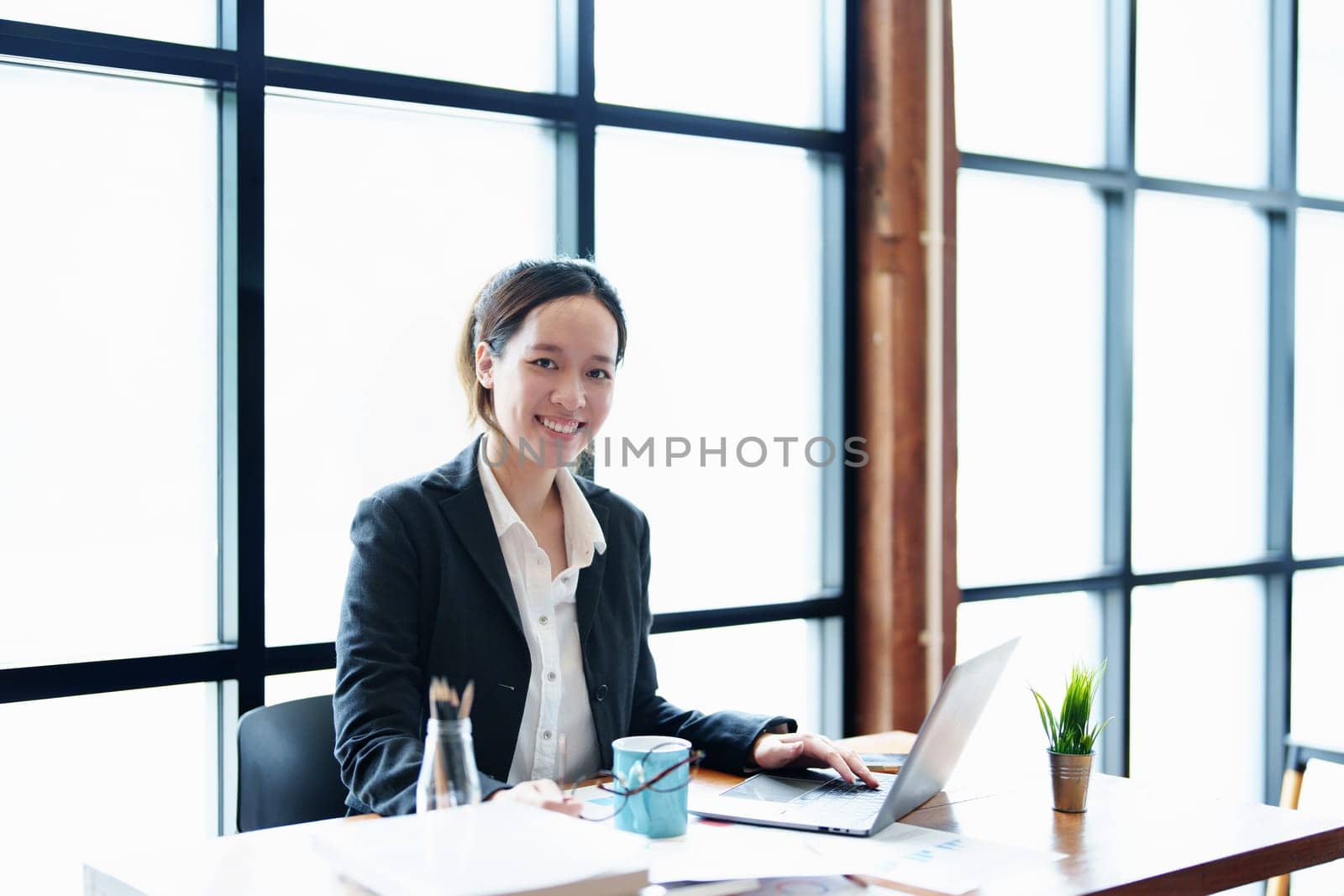 Portrait of a young Asian woman showing a smiling face using a computer and financial statements.