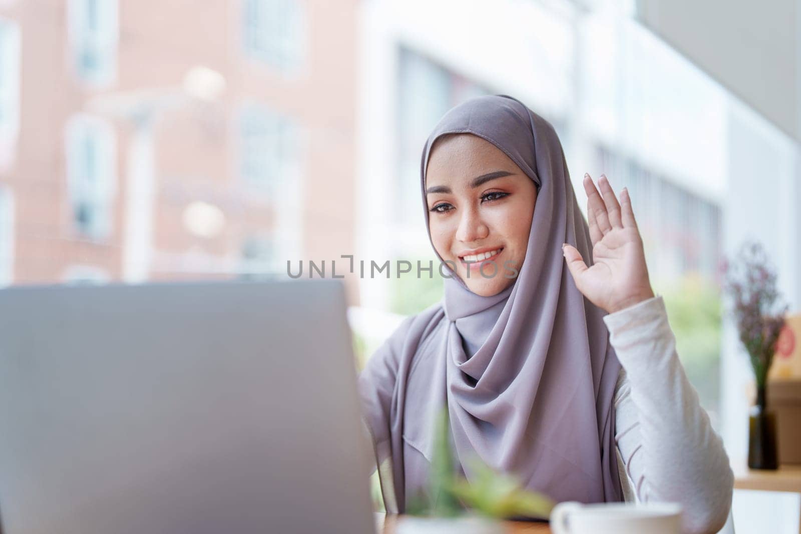 Beautiful Muslim woman using computer to greet attendees via video conference by Manastrong