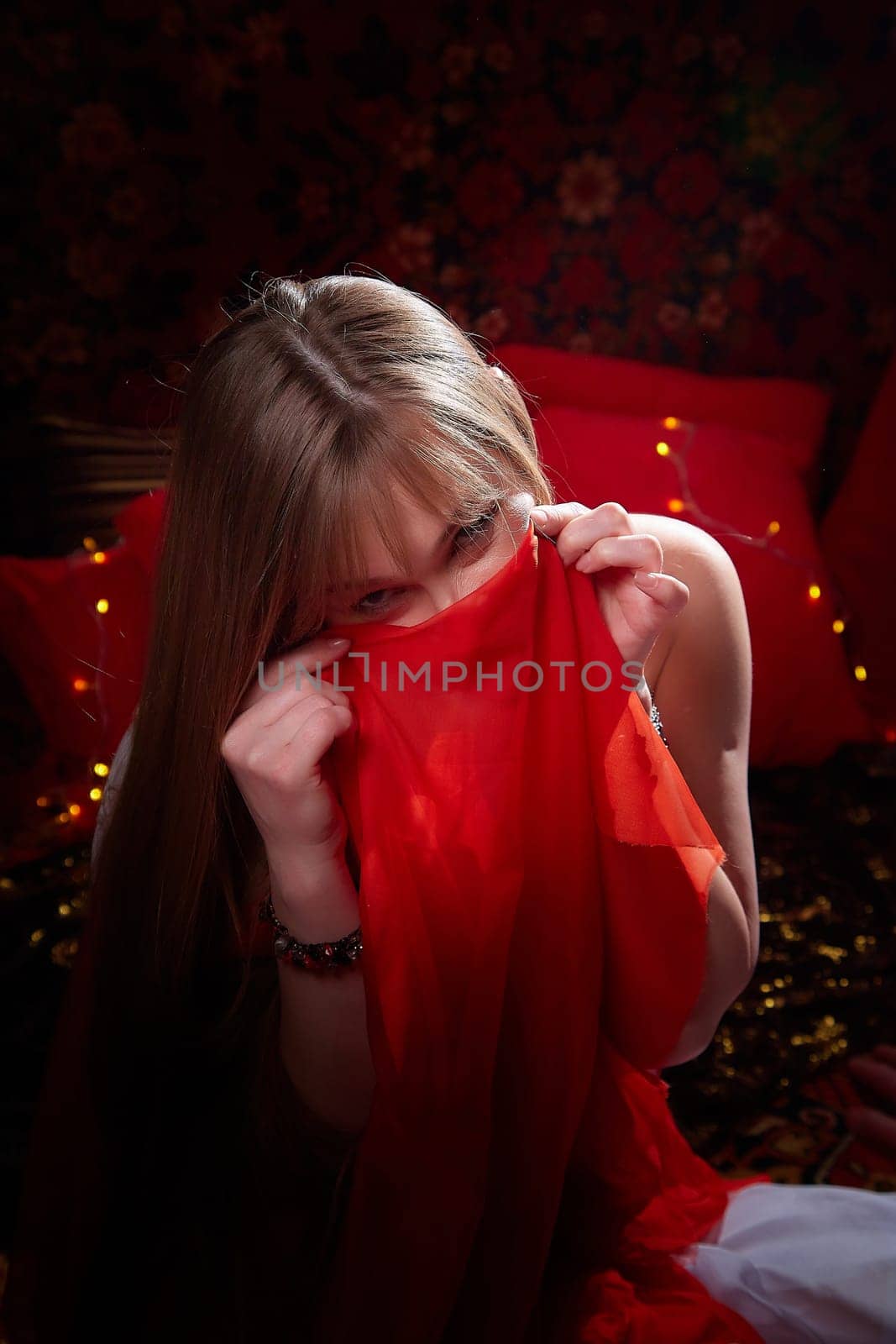 Beautiful European girl looking like Arab woman in red room with rich fabrics and carpets in sultan harem. Photo shoot of an oriental style odalisque. A model poses in sari as indian woman in india